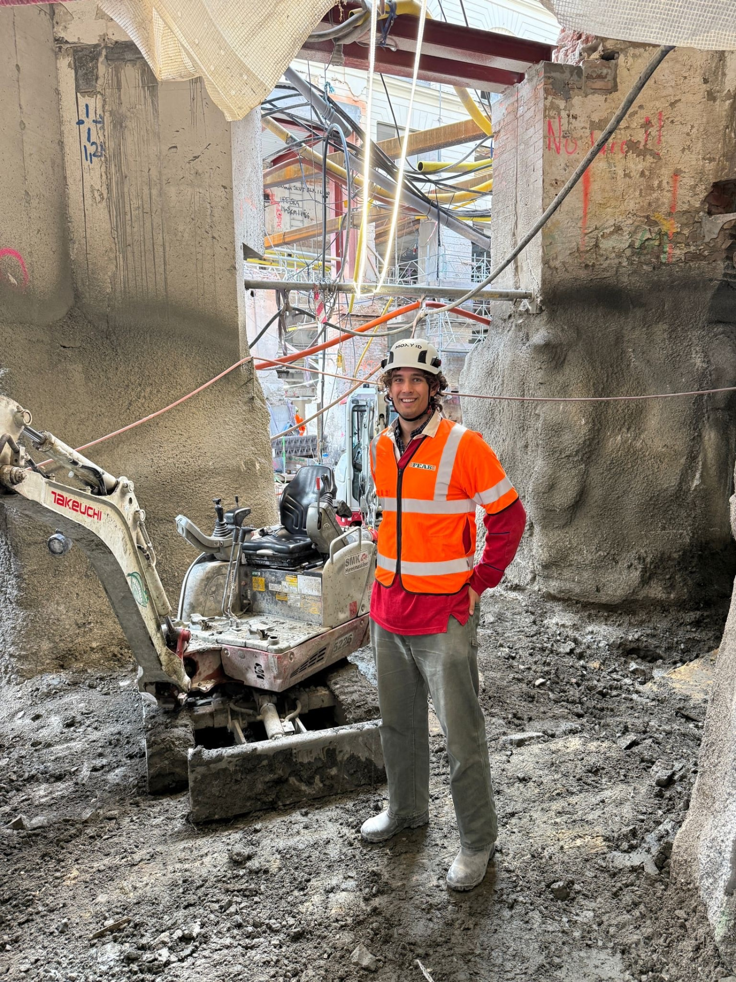 Byggarbetsplats i schakt med grävmaskin i pågående stadsmiljö
